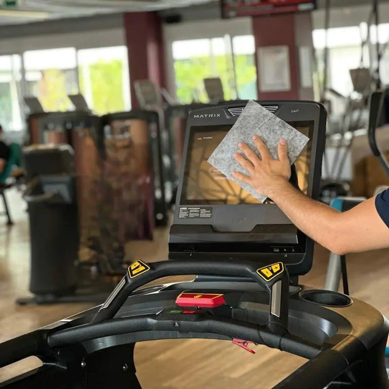 Anwendung der ECO-WIPES Desinfektionstücher im Fitnessstudio – Reinigung eines Touchscreens auf einem Laufbandgerät mit alkoholfreiem Tuch